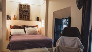 A bedroom with a bed, pillows, a bedside table, a chair, and a door. - Riad Dar Lalla (Marrakech)