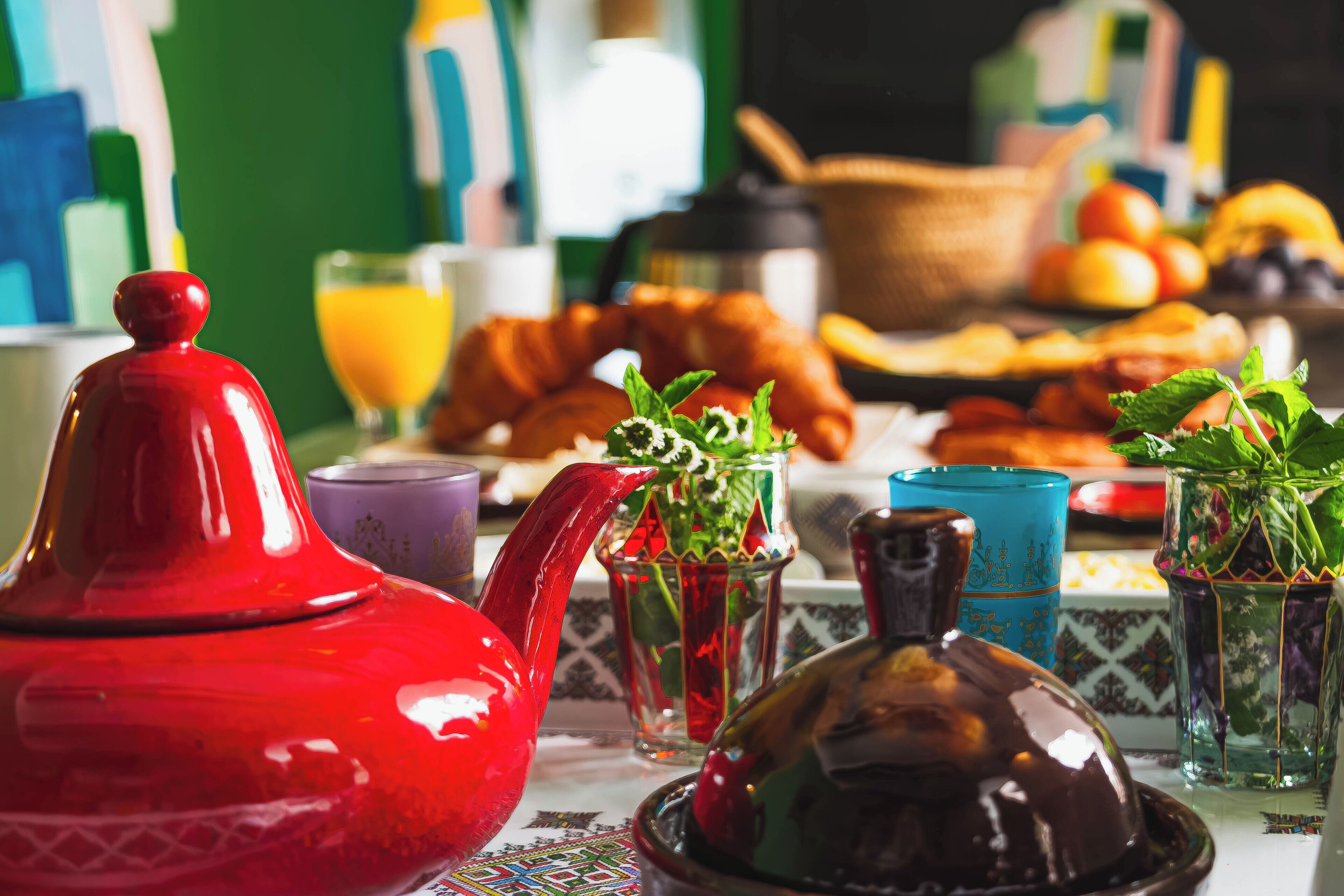 Una tavola imbandita per la colazione, con un bollitore rosso, un brocchetta e diversi tipi di frutta e dolci.