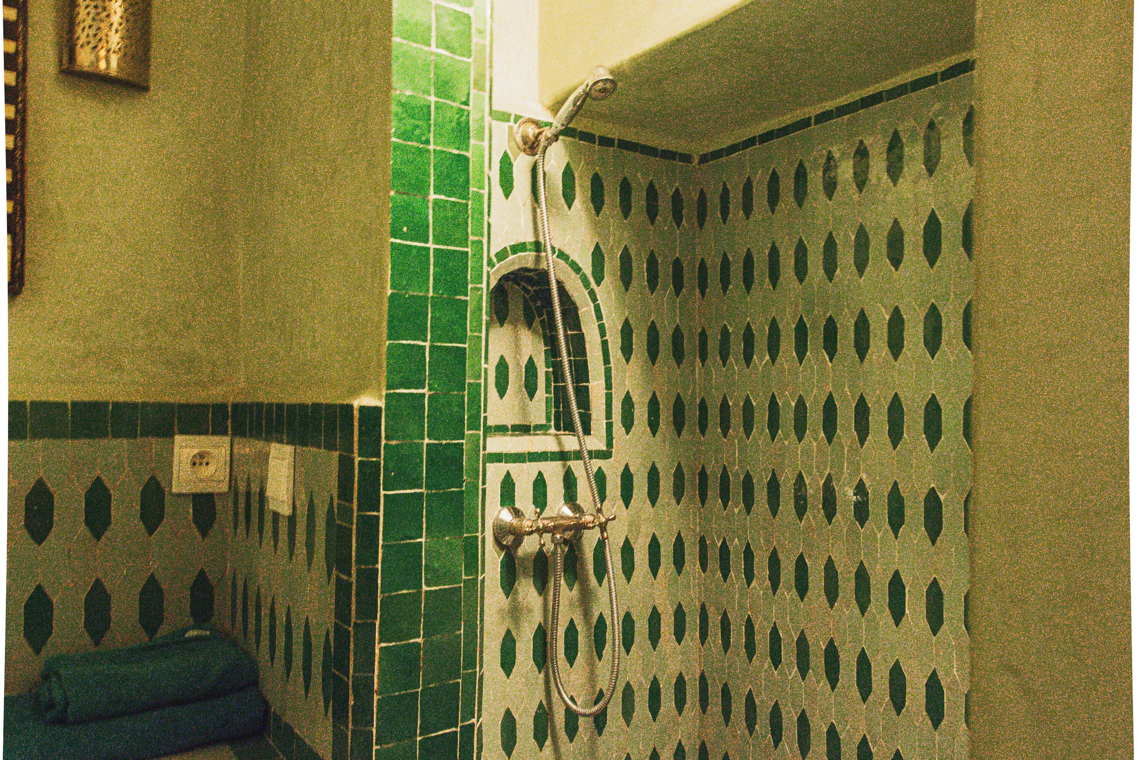 A bathroom with green patterned tiles, a shower with a handheld showerhead, and a towel rack.