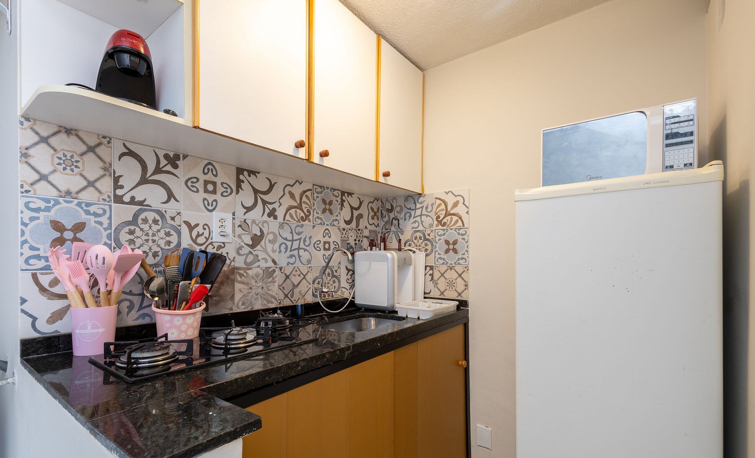 Une cuisine avec des carreaux décoratifs, une cuisinière à gaz, un four à micro-ondes et un réfrigérateur.