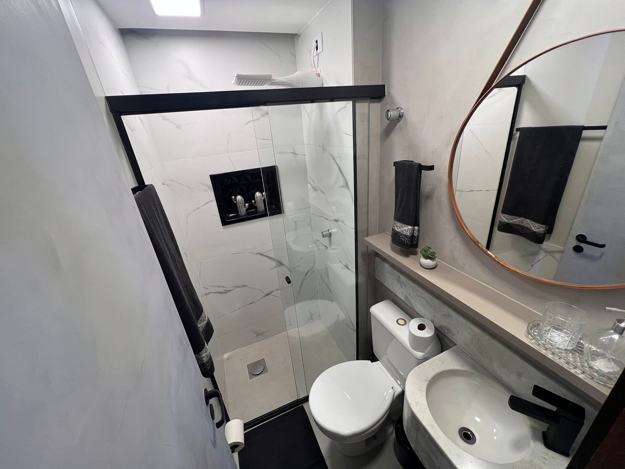 A modern bathroom with a glass shower enclosure, a toilet, a sink, and a mirror with a gold frame.