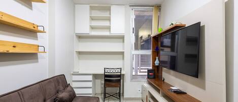 A compact living space with a sofa, a TV, a desk, and built-in shelving.