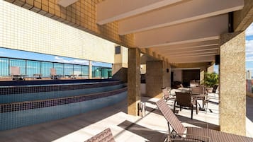 Uma área de piscina no terraço com espreguiçadeiras e vista para o mar.