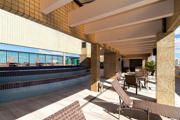 A rooftop pool area with lounge chairs and a view of the ocean.