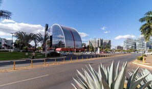 Un edificio moderno con techo curvo, rodeado de palmeras y un cielo despejado.