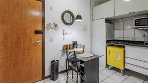 A compact kitchen with a wooden door, a small dining table with chairs, a yellow refrigerator, and a microwave. - Charming Apartment in Asa Norte, Brasilia Gpk0115 (Brasília)