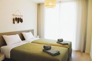 Quarto de hotel com duas camas, um candeeiro pendente e uma janela com cortinas.