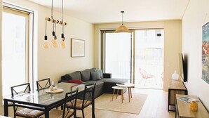 Un salon moderne avec une table à manger en verre, un canapé gris et une grande fenêtre donnant sur la ville.