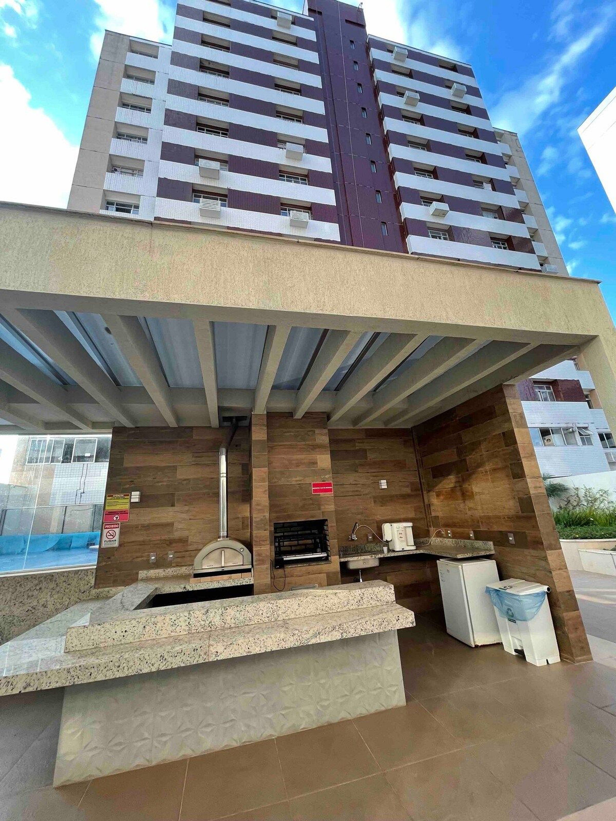 Un edificio moderno con una zona de bar en la azotea que cuenta con una parrilla, asientos y vistas de la ciudad.