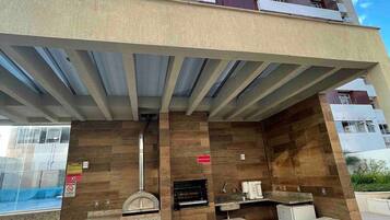 Un edificio moderno con una zona de bar en la azotea que cuenta con una parrilla, asientos y vistas de la ciudad.