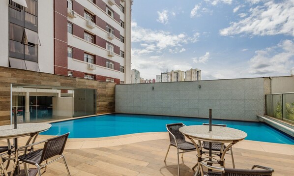 A rooftop pool area with outdoor seating and a view of a high-rise building in the background.