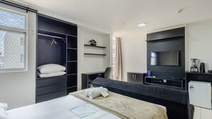 A hotel room with a bed, a desk, a wardrobe, a TV, and a mini-fridge. - Beautiful Studios in Condominium With Pool - Aguas Claras - Madb (Águas Claras)