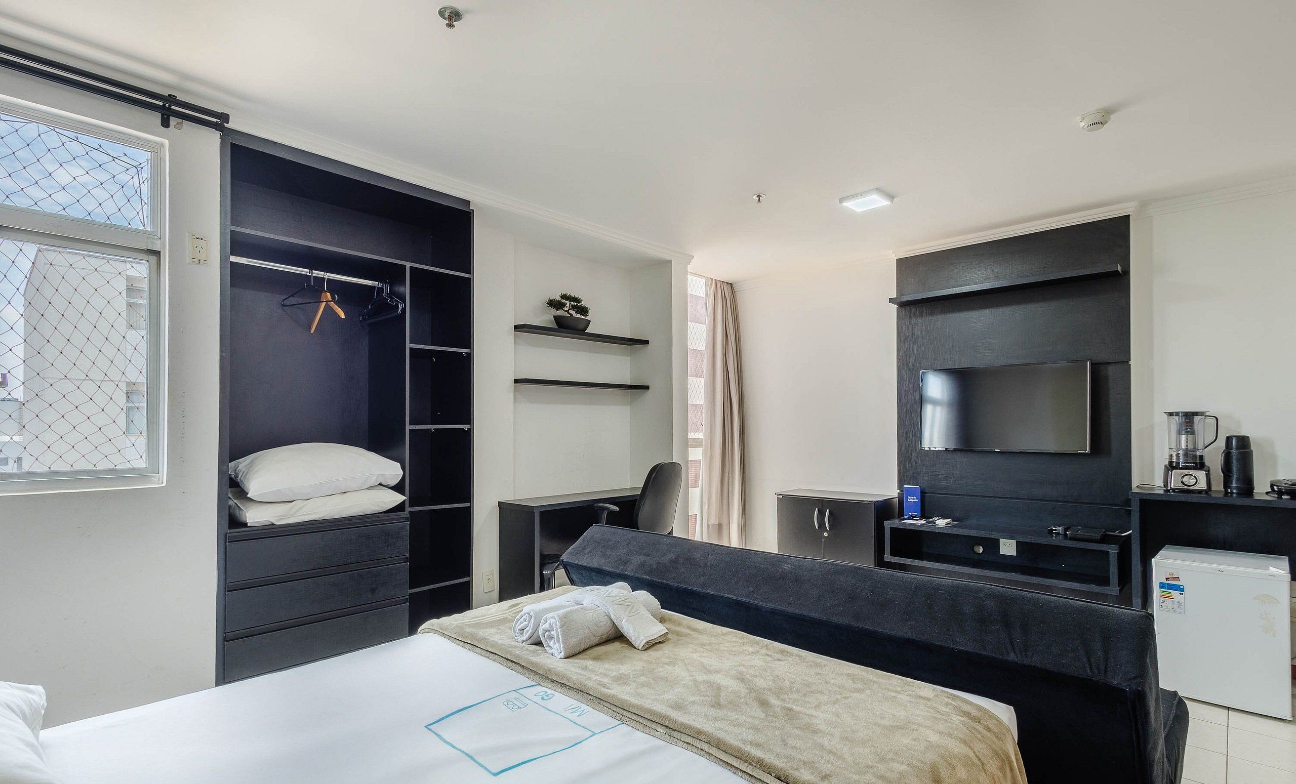 A hotel room with a bed, a desk, a wardrobe, a TV, and a mini-fridge.