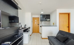 A modern kitchen with a microwave, toaster, and coffee maker. There is a black sofa and a wooden door in the living area. - Beautiful Studios in Condominium With Pool - Aguas Claras - Madb (Águas Claras)