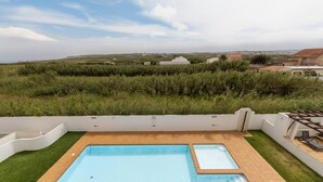 Una piscina rectangular amb una zona enrajolada, envoltada per un mur blanc i una zona verda.
