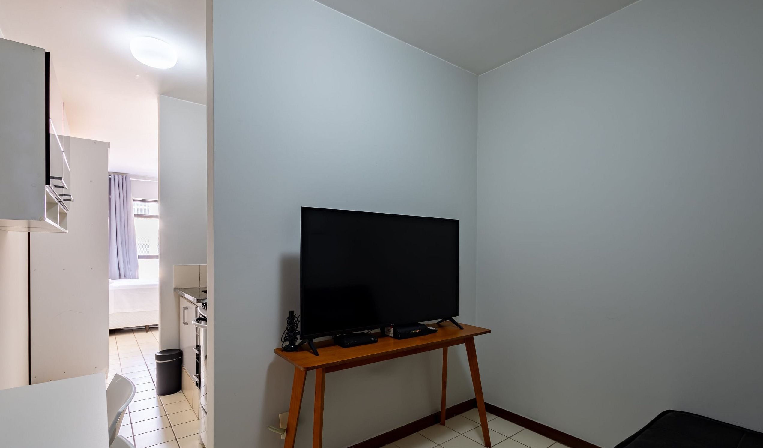 A room with a television on a wooden stand, a white wall, and a door leading to another room.