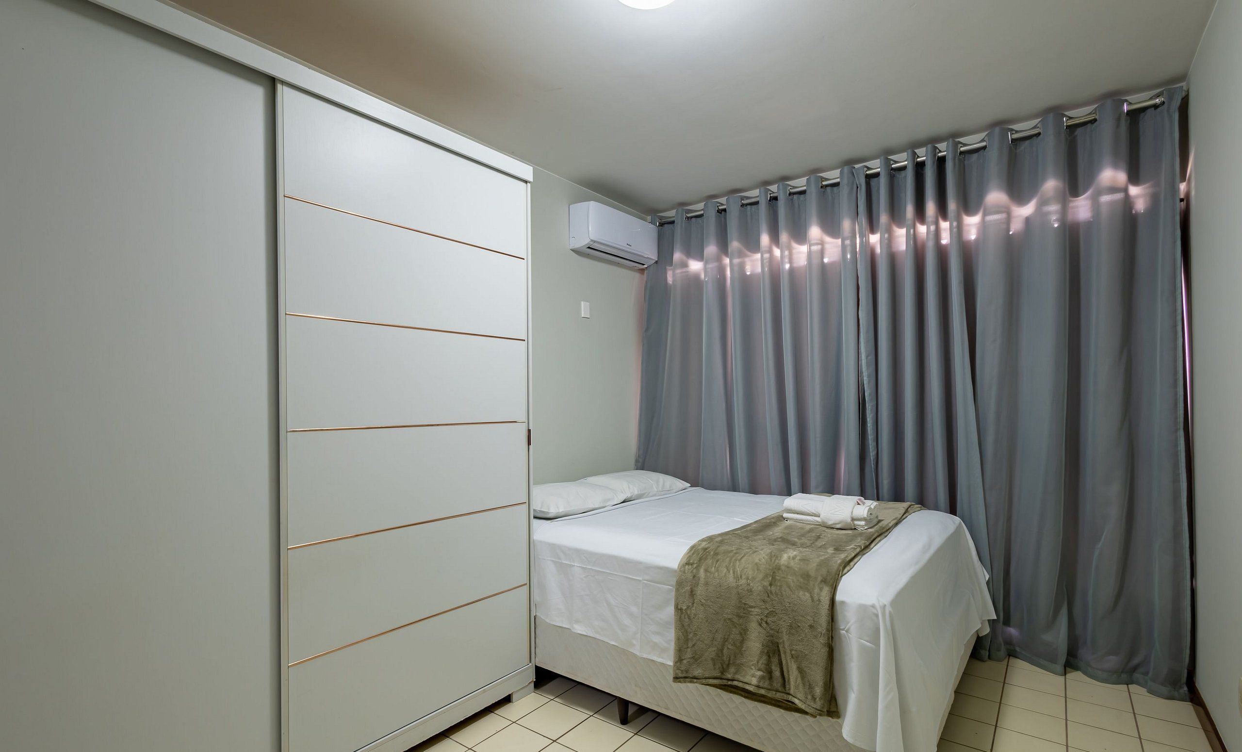 Een slaapkamer met een bed, een kledingkast, een airconditioner en grijze gordijnen.