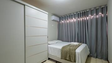 Een slaapkamer met een bed, een kledingkast, een airconditioner en grijze gordijnen.