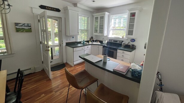 A kitchen with white cabinets, a black countertop, and a stove. There are two brown chairs and a small table. - Cozy townhouse minutes from downtown Portland on a car free island (Portland)