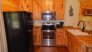 A kitchen with wooden cabinets, a stainless steel refrigerator, a microwave, a stove, and a sink. - White Potato Lake Cabin Retreat (Pound)