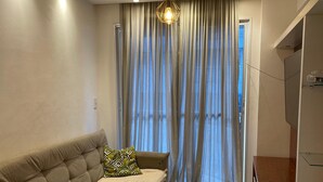 A modern living room with a sofa, a hanging light fixture, and a view through sheer curtains. - Luxury apartment in Maracanã (São Francisco Xavier Rio de Janeiro)