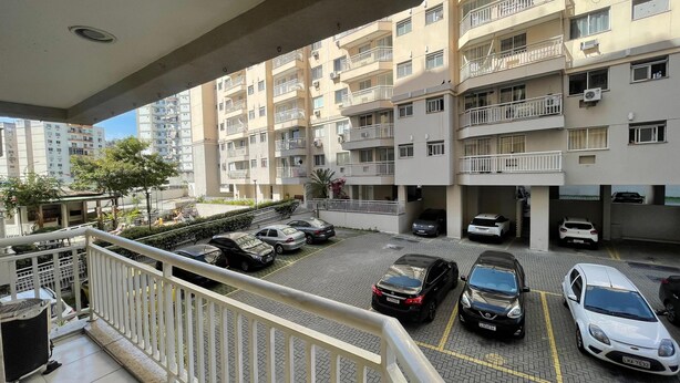A multi-story residential building with balconies, a parking area with several cars, and a view of a street with other buildings. - Luxury apartment in Maracanã (São Francisco Xavier Rio de Janeiro)