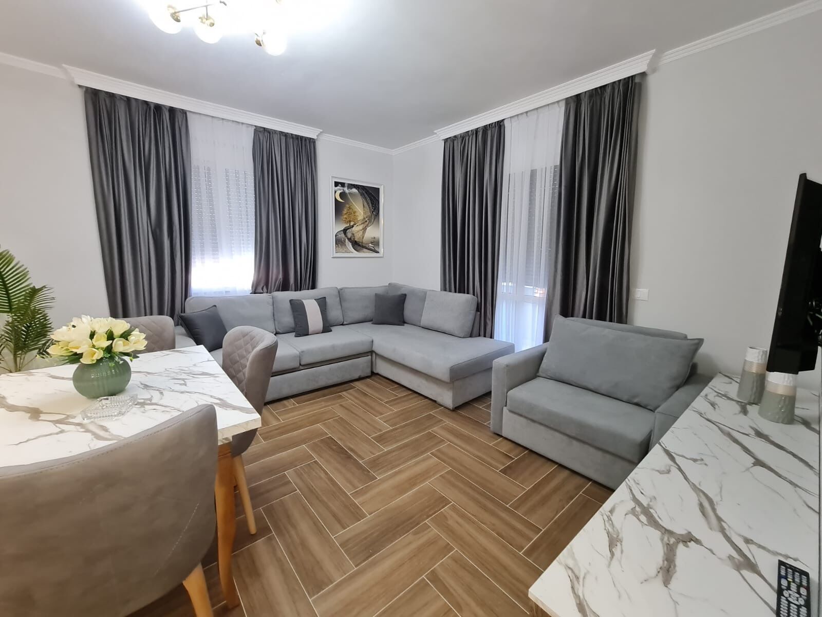 A modern living room with a sectional sofa, a dining table with chairs, and a TV on a stand.