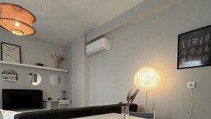 A modern living room with a white table and chairs, a black sofa, a hanging light fixture, and a wall-mounted air conditioner. - A-Chic 1-bedroom apartment with WiFi, AC in vibrant Istanbul (İstanbul)