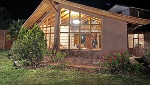 A house with a large glass window, a wooden roof, and a garden with plants and flowers. - Andean Cottage w/ Garden & Workspace near Urubamba (Urubamba)