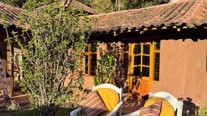 Two white chairs with yellow cushions and striped pillows outside a building with a tiled roof. - Andean Cottage w/ Garden & Workspace near Urubamba (Urubamba)
