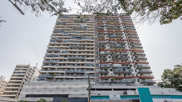 A multi-story residential building with balconies, a visible parking garage, and a sign indicating a parking area. - Noas - Apartments in the South Zone of SP (São Paulo)
