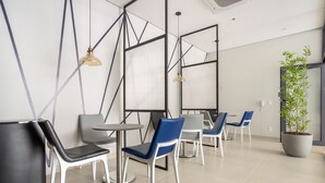 A modern interior with a seating area featuring white and blue chairs, a round table, and pendant lighting. - Noas - Apartments in the South Zone of SP (São Paulo)