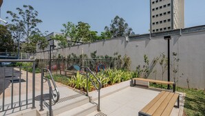 A public outdoor area with a metal fence, steps leading to a platform, and a bench. - Noas - Apartments in the South Zone of SP (São Paulo)