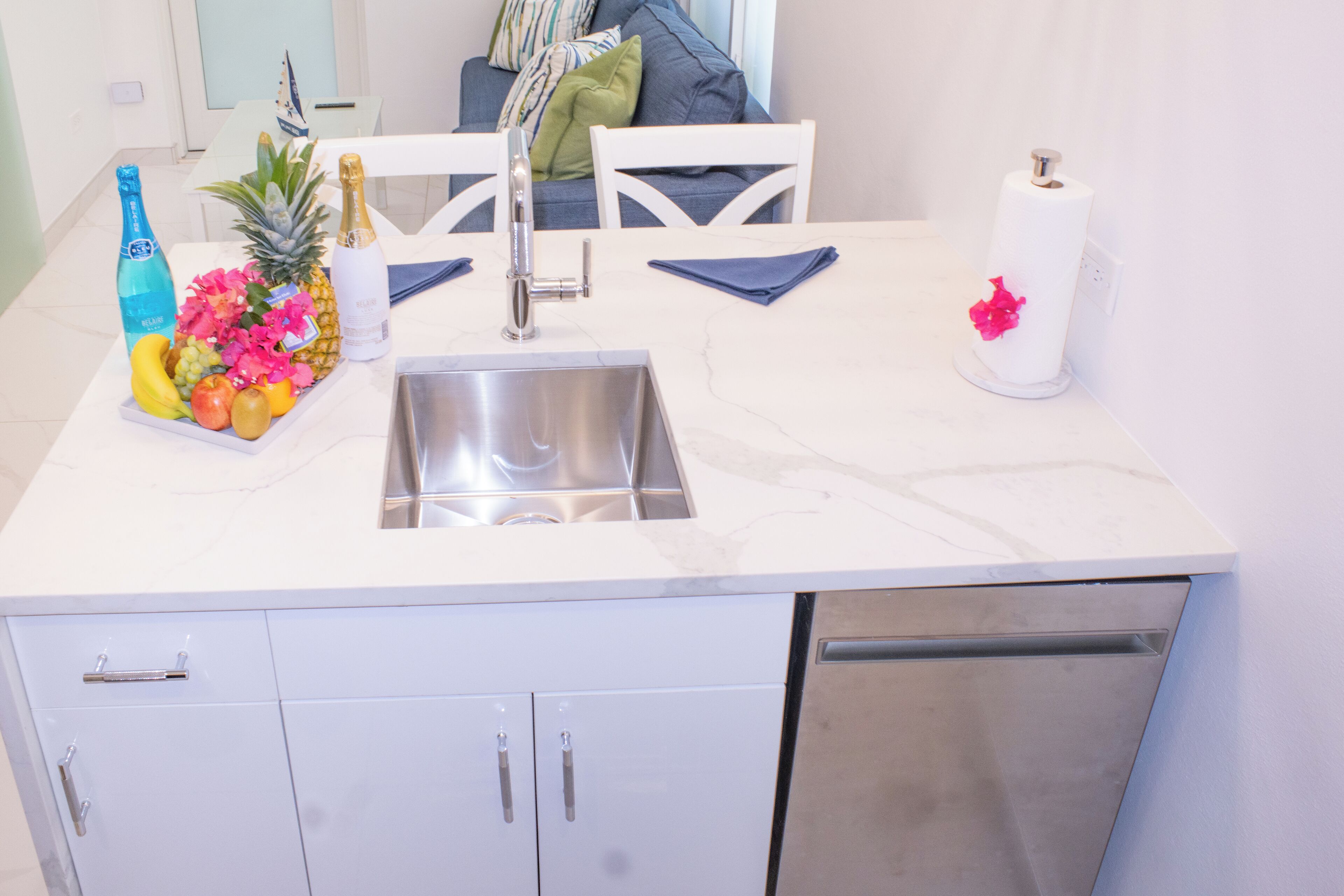A kitchen with a stainless steel sink, white cabinets, and a marble countertop.