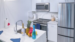 A modern kitchen with white cabinets, stainless steel appliances, a marble countertop, and a small island with a sink and a bottle of water. - Raintree Suites (St. John)