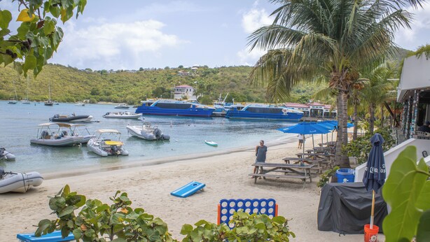 A beach with boats, a palm tree, and a building with a red roof. - Raintree Suites (St. John)