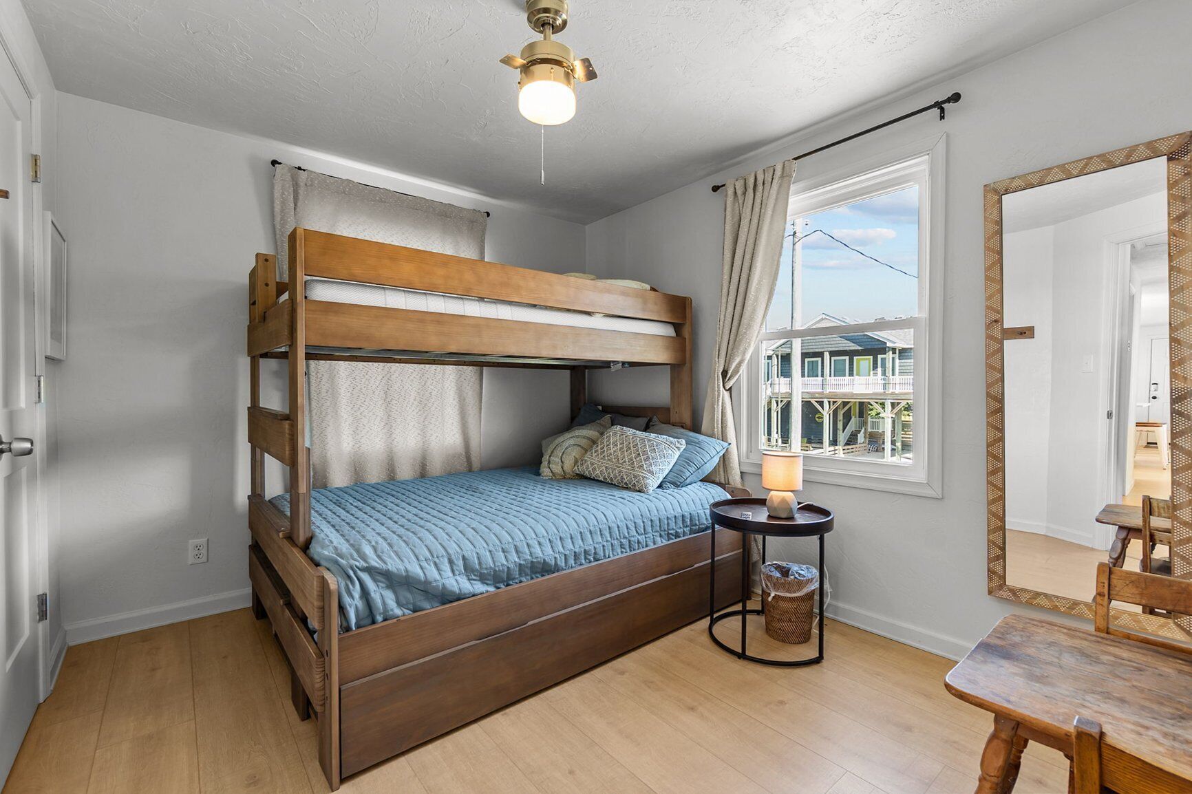 A bunk bed with a blue bedspread, a bedside lamp, and a window with a view of a balcony.