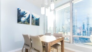 A modern dining area with a wooden table and chairs, large windows with a city view, and two abstract paintings on the wall. - Luxury Executive Downtown 1 bedroom Suite (Vancouver)