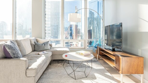 A modern living room with a sofa, a coffee table, a TV on a wooden stand, and large windows offering a city view. - Luxury Executive Downtown 1 bedroom Suite (Vancouver)