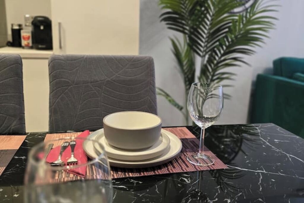 Una mesa de comedor con un tazón, una copa de vino y cubiertos sobre una superficie de mármol negro.