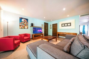 A modern living room with a large grey sofa, red armchairs, a wooden coffee table, a flat-screen TV, and artwork on the walls.