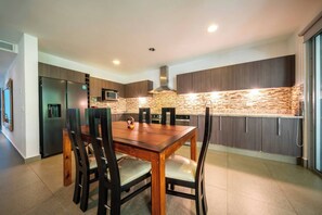 A modern kitchen with a wooden dining table and chairs, built-in appliances, and a stone backsplash.