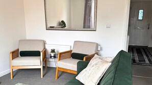 Un salon avec deux fauteuils, un canapé vert, un grand miroir et une petite table sur laquelle est posée une plante.