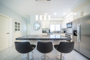 A modern kitchen with a central island, bar stools, stainless steel appliances, and a decorative clock.