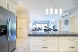 A modern kitchen with a stainless steel refrigerator, granite countertops, white cabinetry, and pendant lighting.