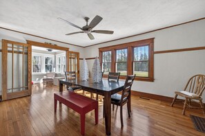A dining area with a wooden table, chairs, a red bench, a ceiling fan, and large windows with a view of trees. - THE CHRISTMAS HOUSE! 20 ACRES ON A X-MAS TREE FARM!! YEAR ROUND CHRISTMAS DECOR (Roscoe)