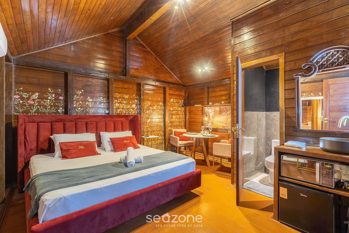 A wooden cabin-style room with a large bed, a small table with chairs, a sink, and a mirror.