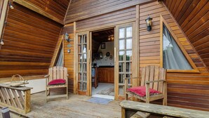 A wooden cabin with a loft bedroom, a kitchen, and two wooden chairs with red cushions. - Fully Equipped Studios Near Armacao Beach and Beto Carrero Park - TRS (Penha)
