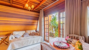 A cozy room with a wooden ceiling, a bed with patterned bedding, a dining table set with plates, glasses, and a teapot. - Fully Equipped Studios Near Armacao Beach and Beto Carrero Park - TRS (Penha)