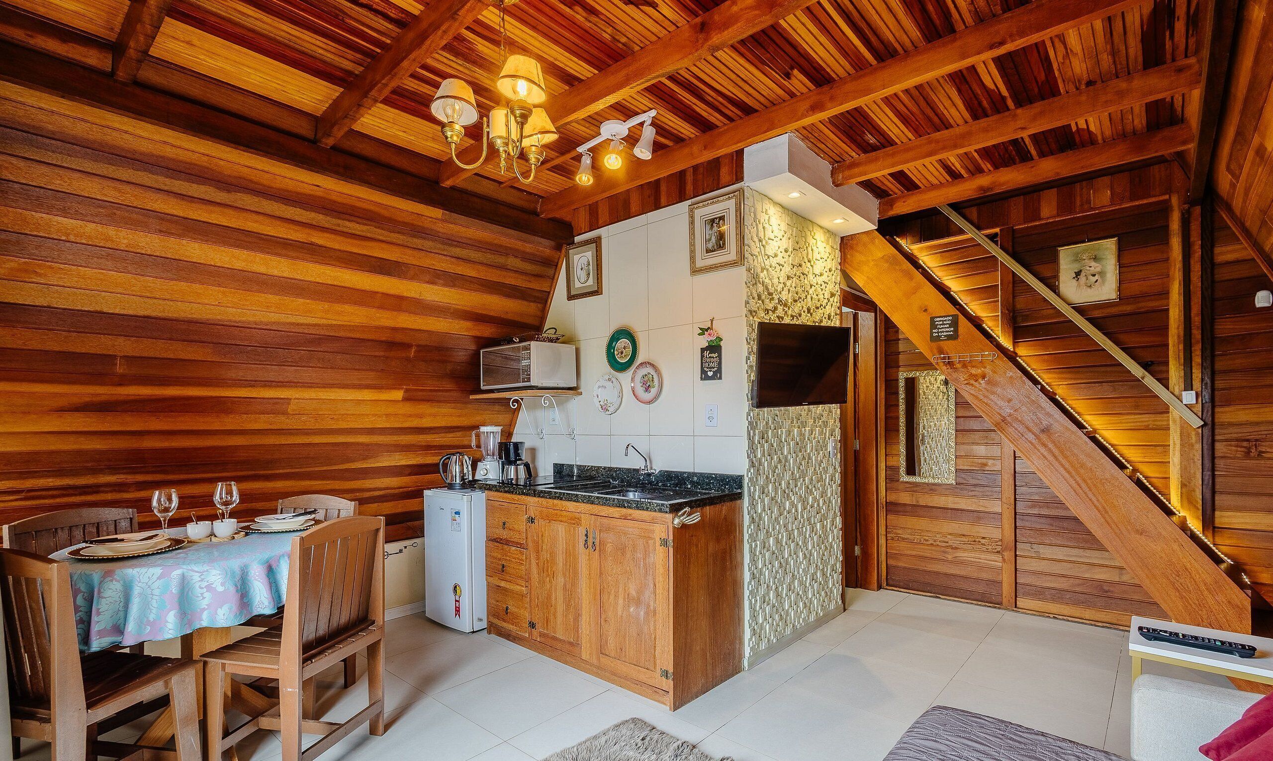 Interior em madeira com cozinha, mesa de jantar e escada.